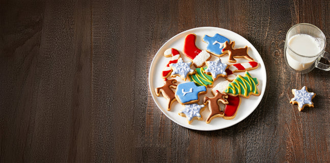 Decorative cookies shaped like animals on a plate with a glass of milk on a wooden table.
