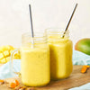 Two mason jars filled with a yellow smoothie with metal straws sticking out of them.