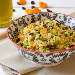 A bowl of couscous with dried apricots pistachios and cranberries.