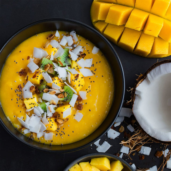 A bowl of mango smoothie topped with coconut flakes kiwi and chia seeds.