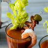 A close-up of a bloody mary cocktail garnished with celery bacon a shrimp and an olive.