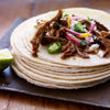 A stack of tortillas topped with shredded meat onions peppers and cheese.