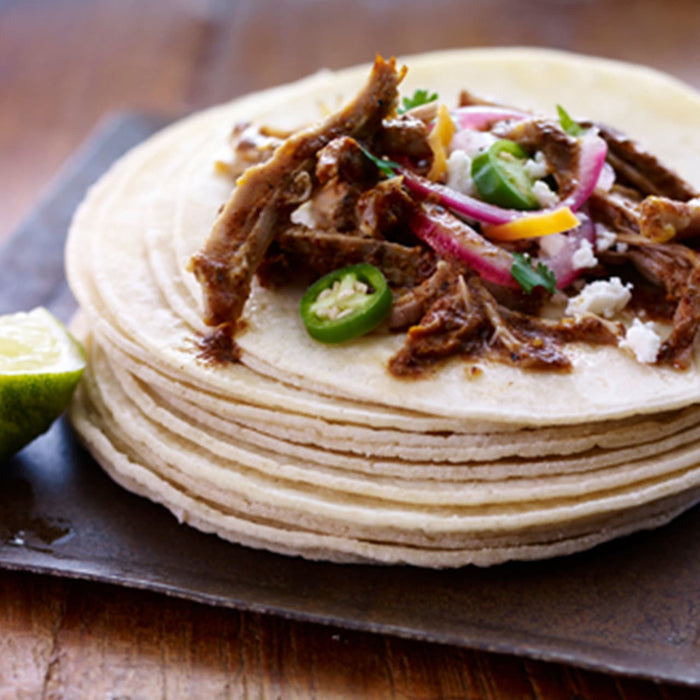 A stack of tortillas topped with shredded meat onions peppers and cheese.