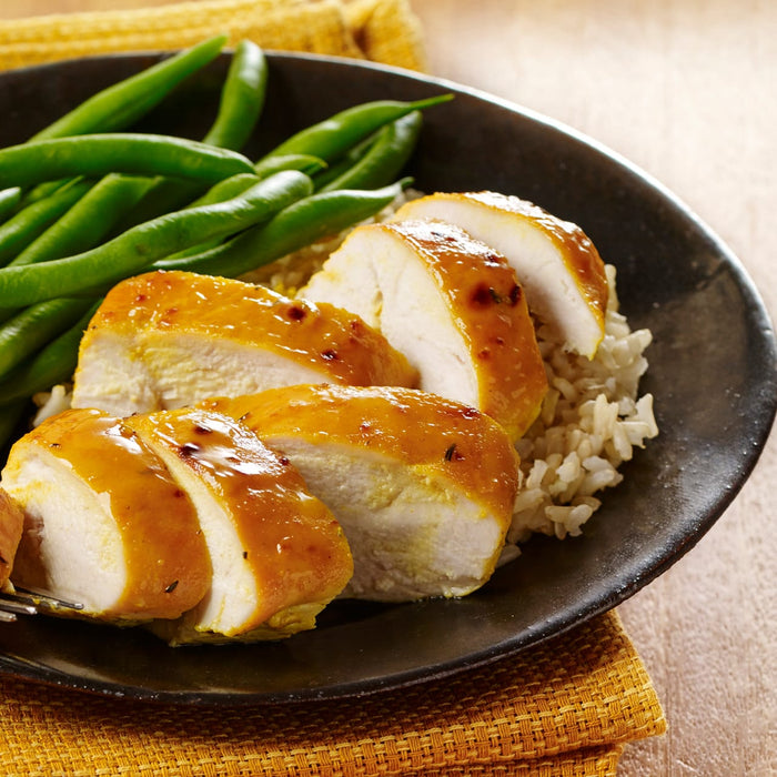 A plate of sliced chicken breast with a yellow sauce green beans and rice.