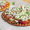 A grilled flatbread topped with feta cheese tomatoes onions and fresh herbs.