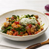 A bowl of hearty stew with a dollop of creamy sauce and cucumber slices on top.