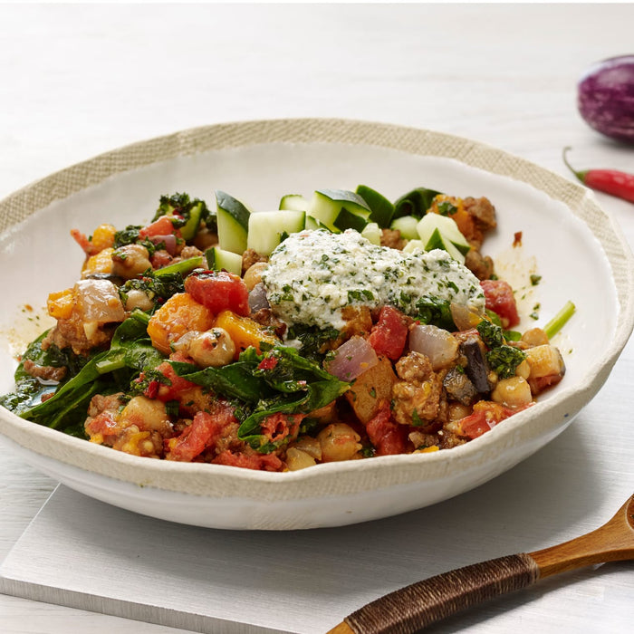 A bowl of hearty stew with a dollop of creamy sauce and cucumber slices on top.