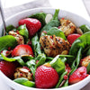 A bowl of spinach salad with strawberries chicken and almonds.