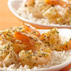 A plate of white rice topped with shrimp and a lemon butter sauce.
