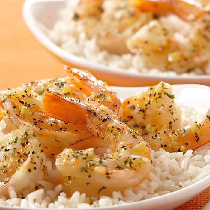 A plate of white rice topped with shrimp and a lemon butter sauce.