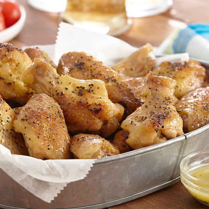 A close-up of a metal bowl filled with roasted chicken wings.