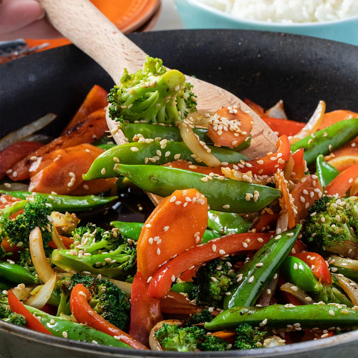A close-up of a pan of stir-fried vegetables with sesame seeds.