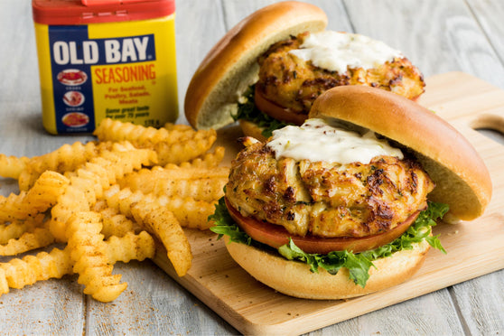 old bay crab cake on a bun with french fries on the side sitting on a wooden cuting board