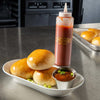 Three buns, a small bowl of sauce, and a bottle of Cattlemens BBQ sauce on a metal counter.