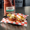 A bottle of Cattlemens BBQ Sauce with two Hawaiian Tangy Sweet BBQ sliders on a red and white checkered paper.