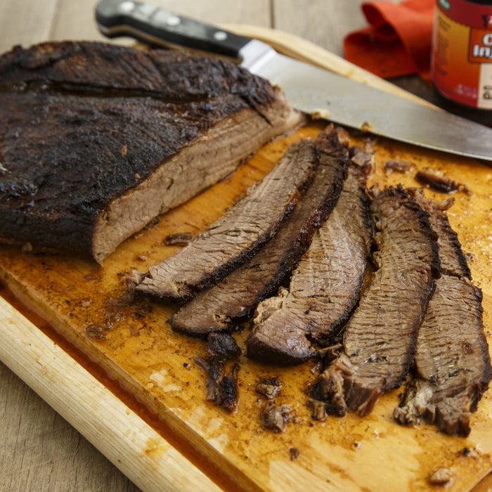 A sliced brisket sits on a wooden cutting board with a knife, ready to be served.
