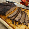 A sliced brisket sits on a wooden cutting board with a knife, ready to be served.