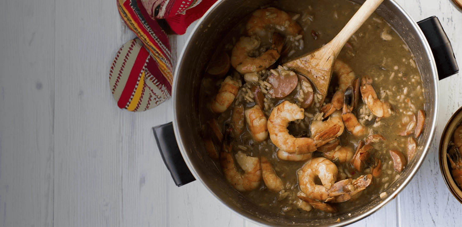 Prawns cooking in a pan with a wooden spoon on a light wooden surface.