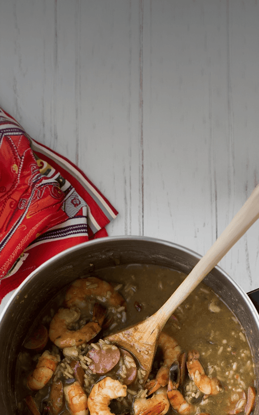 Pot of shrimp and grits with a wooden spoon on a white background