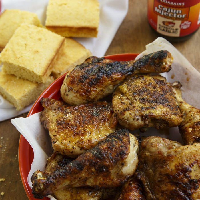 A plate of grilled chicken and cornbread is shown with Zatarains Cajun Injector Creole Garlic marinade.