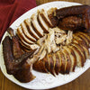 A platter of sliced and shredded smoked turkey is displayed on a wooden table with a red cloth.