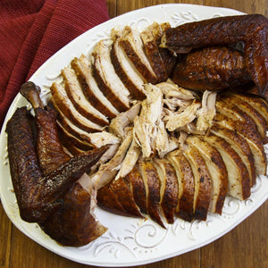 A platter of sliced and shredded smoked turkey is displayed on a wooden table with a red cloth.