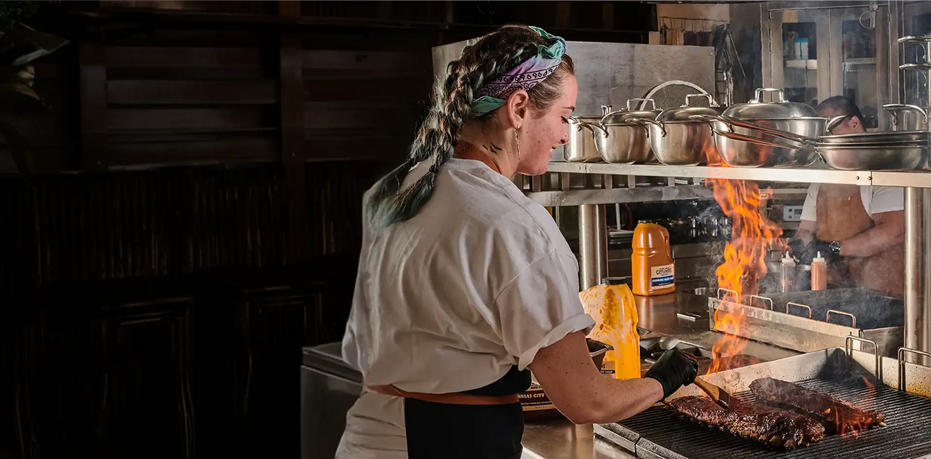 Person cooking over a flaming grill in a professional kitchen