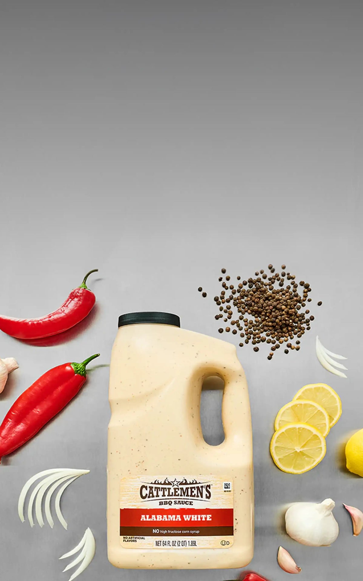 Cattlemen's Alabama White sauce bottle with peppers, lemon slices, and garlic on a gray background