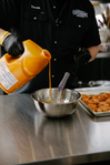 Chef in a Cattlemen’s shirt pouring orange sauce from a large jug into a mixing bowl beside a tray of shrimp.