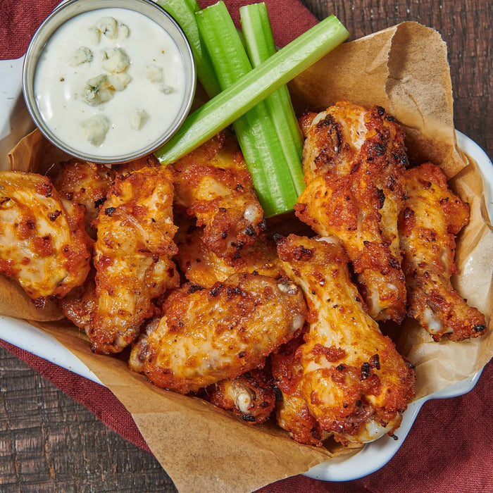 A plate of crispy chicken wings with celery sticks and blue cheese dip.