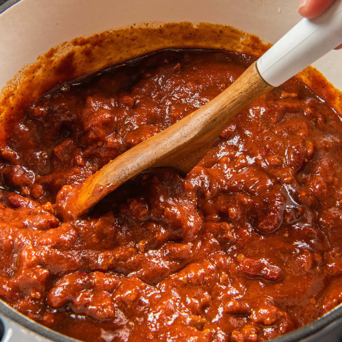 A close-up of a pot of chili with a wooden spoon in it.