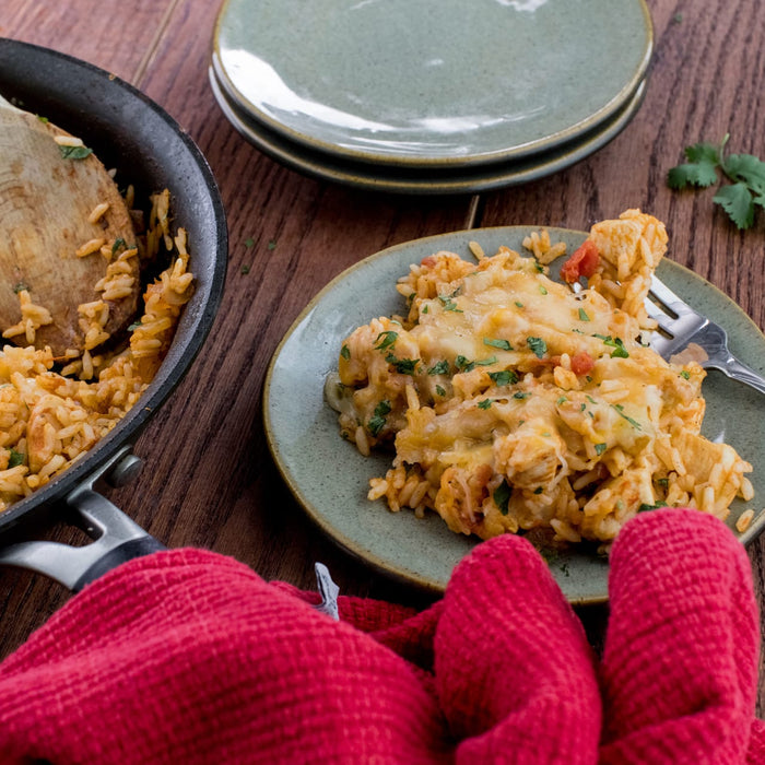 A plate of cheesy chicken and rice with a red potholder and a wooden spoon in the background.
