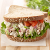 A chicken salad sandwich on a whole wheat roll with lettuce, tomato, and red onion.