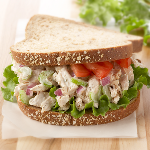 A chicken salad sandwich on a whole wheat roll with lettuce, tomato, and red onion.
