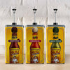 Three large yellow pump dispensers featuring the labels for Cholula Hot Sauce in Chipotle, Original, and Green Pepper varieties are lined up against a white brick wall.