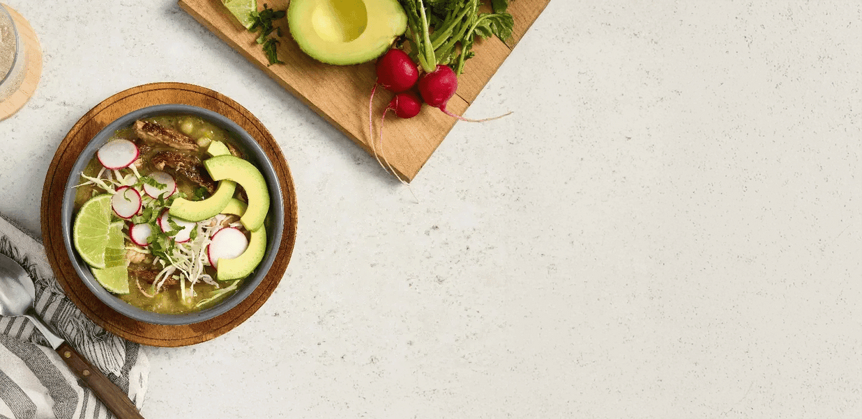 Bowl of soup with avocado and radishes on a light surface