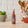 A bottle of Cholula Extra Hot Hot Sauce sits on a countertop with a bowl of limes and a bowl of garlic.