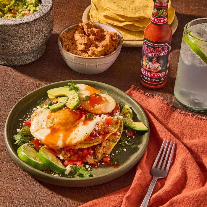 A plate of huevos rancheros with a bottle of Cholula Hot Sauce and a glass of water with a lime wedge.
