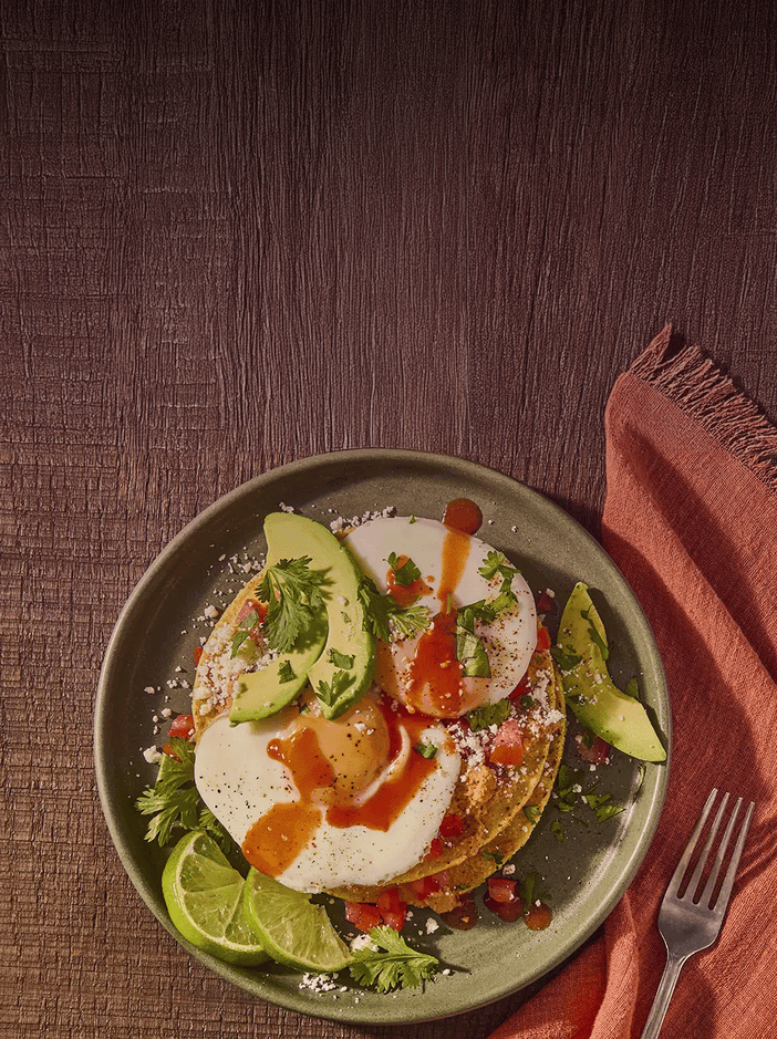 Plated dish of tacos with avocado, lime, and sauce on a wooden table.