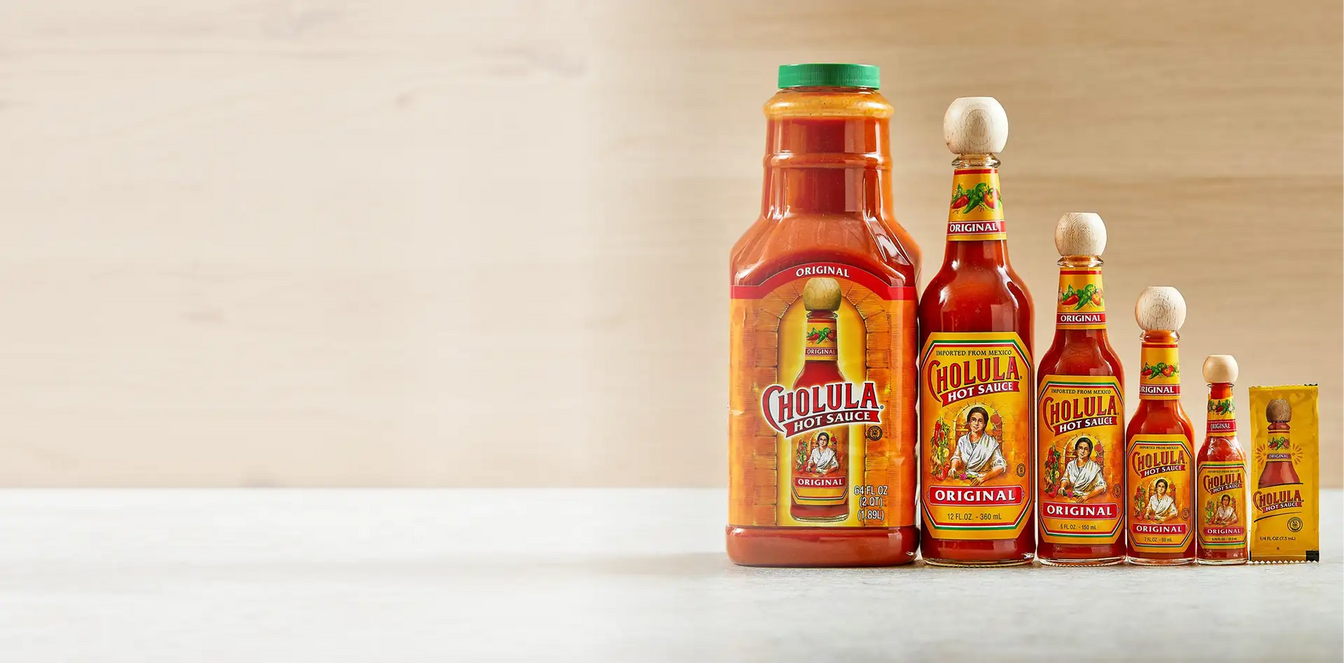Cholula hot sauce bottles of various sizes on a white surface with a beige background