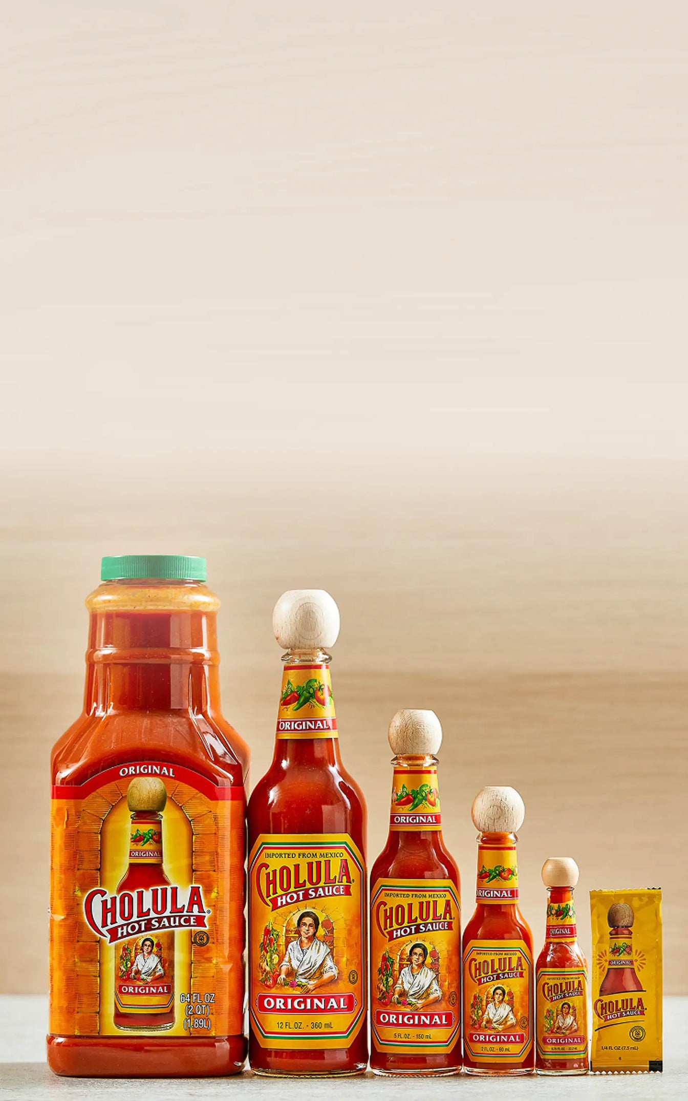 Cholula hot sauce bottles of various sizes on a white surface with a beige background