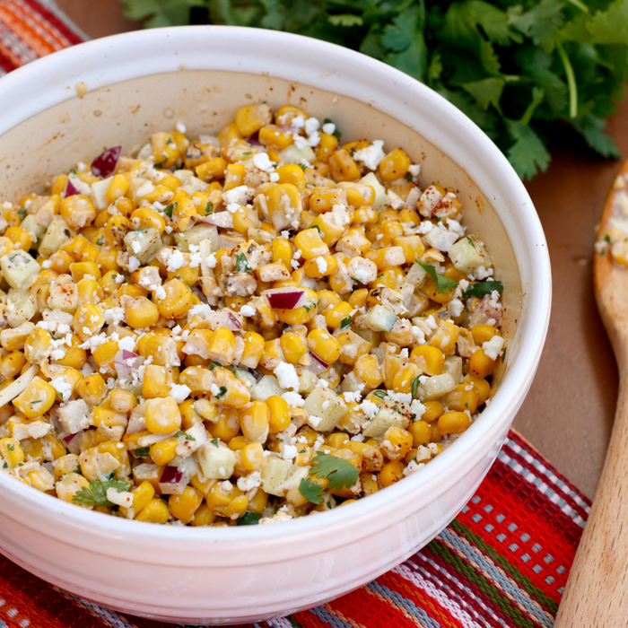 A white bowl filled with a corn salad with feta cheese, red onion, and cilantro.
