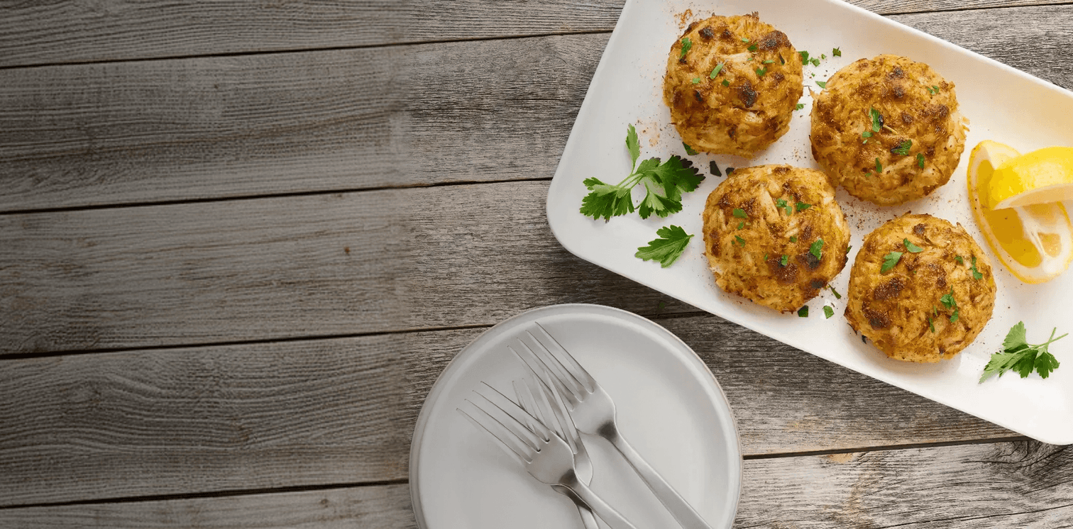 Plated crab cakes on a wooden table with a side of lemon wedges.