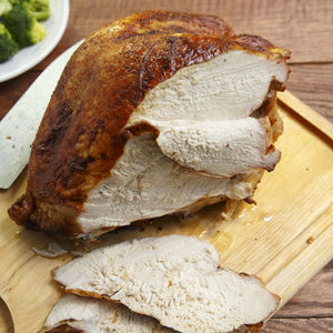 A juicy roasted turkey breast sits on a wooden cutting board, partially sliced and ready to be served.