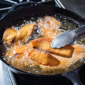 A close-up of a cast iron skillet with fish fillets frying in hot oil.