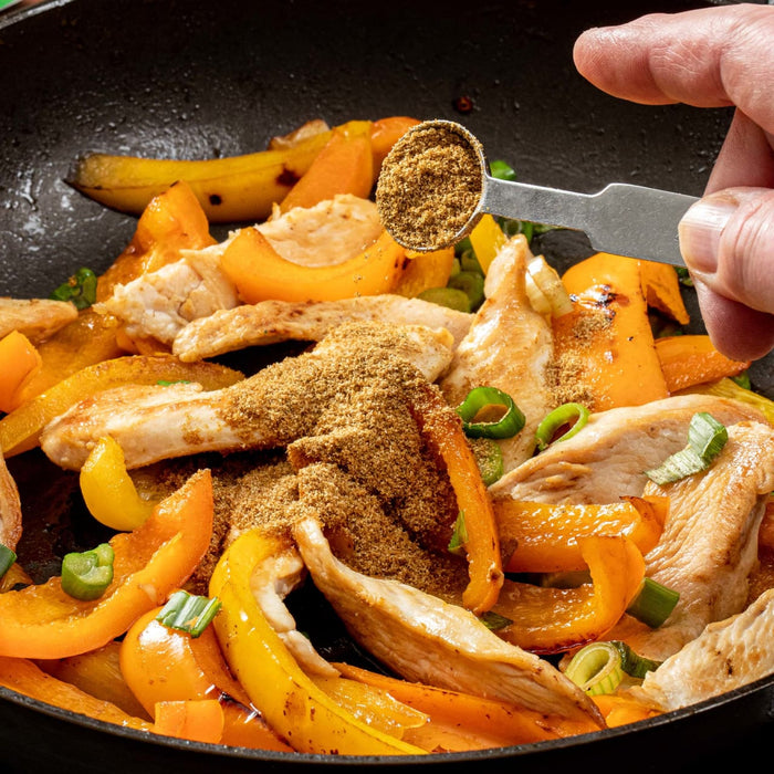 A close-up of a skillet with chicken, peppers, and spices being prepared.