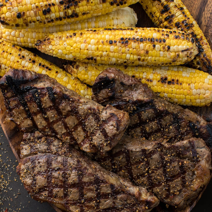 Grilled steaks and corn on the cob are arranged on a wooden platter, showcasing a delicious and hearty meal.