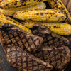 Grilled steaks and corn on the cob are arranged on a wooden platter, showcasing a delicious and hearty meal.