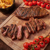 A juicy steak, sliced and served with cherry tomatoes and fries, is presented on a wooden cutting board.