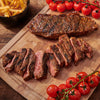 A juicy steak, sliced and served with cherry tomatoes and fries, is presented on a wooden cutting board.